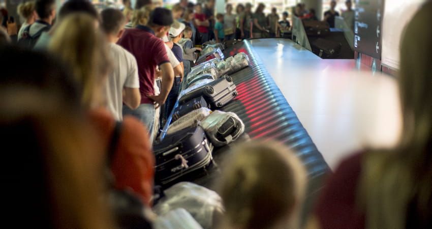 A crowd of people look for luggage at an airport baggage claim