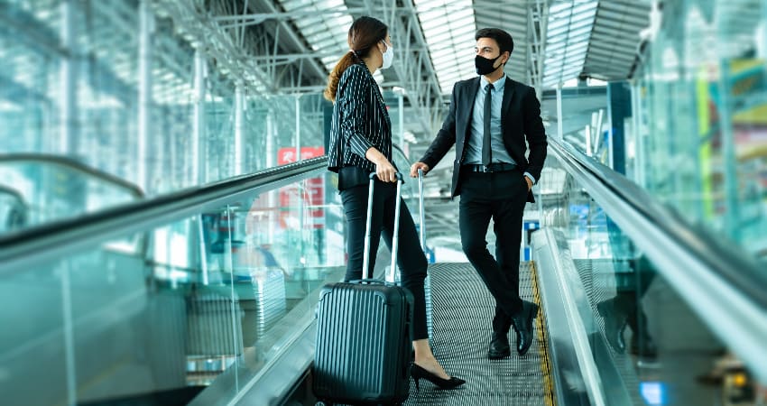 Two businesspeople ride an escalator with luggage in an airport