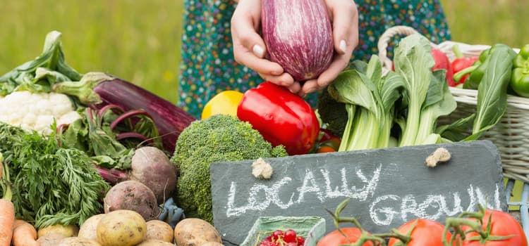 someone holds a vegetable over a table of vegetables with a sign that reads "locally grown"