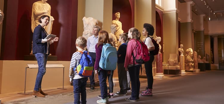 kids with backpacks stand and admire a museum monument while a tour guide explains