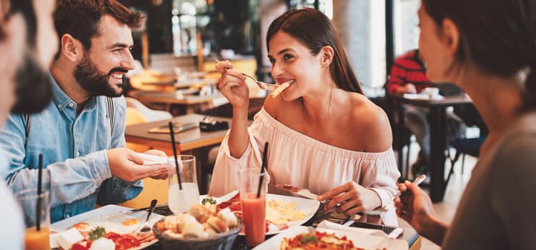 friends sit around a table full of food and smile while drinking