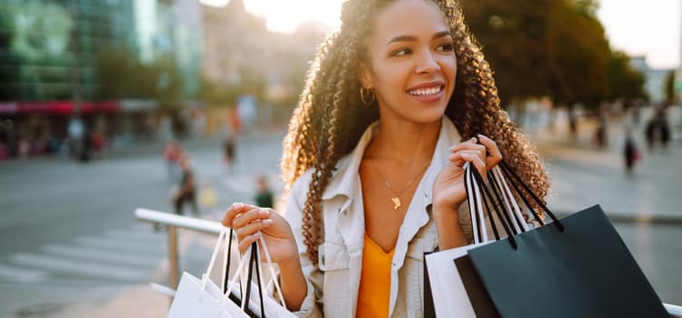 a woman holds two handfuls of shopping bags and smiles