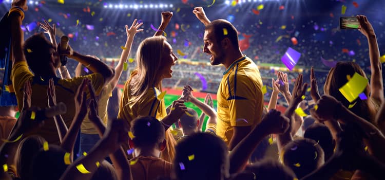 sports fans pump their fists and cheer while an illuminated stadium roars with cheers